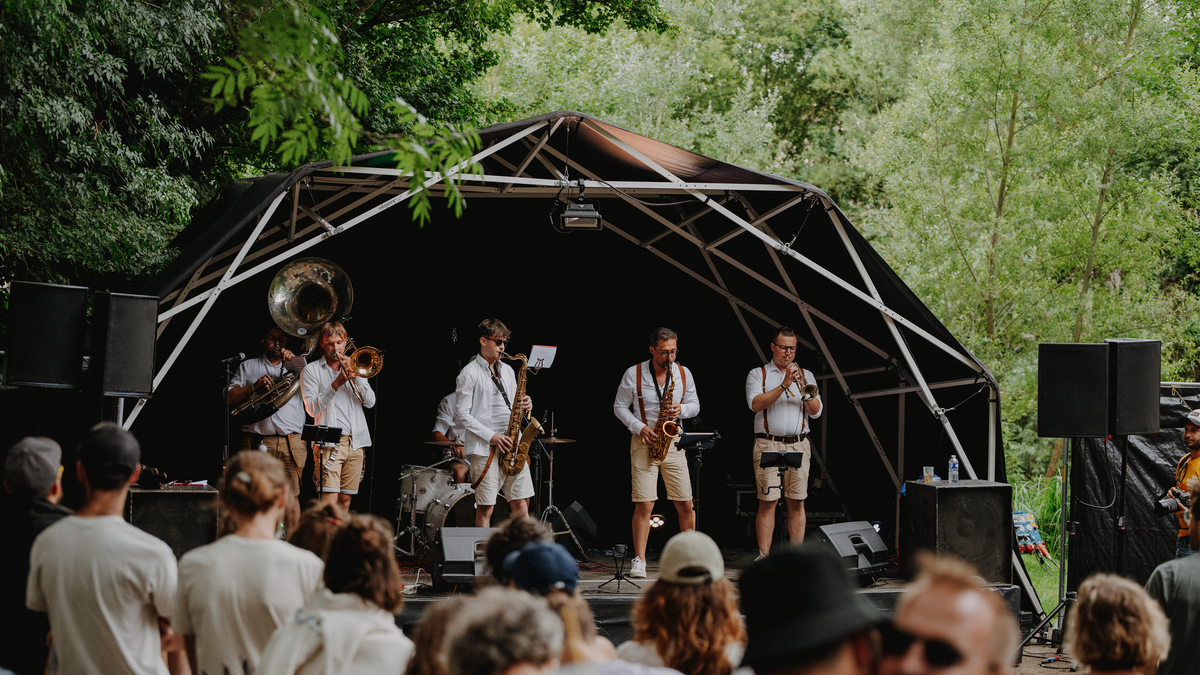 Konligo Fastival event structure with black membrane and outside backdrop hosting a brass band performance at an outdoor festival surrounded by trees, now available on MTN SHOP US.