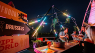 Konligo iluminó la estructura del evento Fastival con plantas colgantes y luces de neón en el bar de la azotea de Bruselas, creando una atmósfera de festival vibrante, ahora disponible en MTN Shop US.