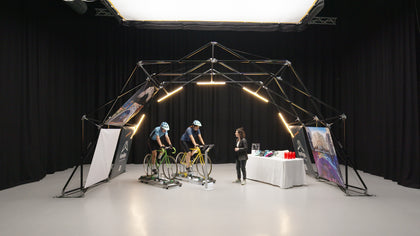 Configuración interior de la estructura para eventos de Konligo con dos ciclistas en bicicletas estáticas y una mesa de exhibición con cascos y botellas de agua. Ahora disponible en MTN Shop EE. UU.
